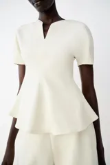Top peplum confeccionado en hilatura de algodón de color bordó, con escote en V pronunciado, mangas cortas abullonadas y bajo con vuelo.