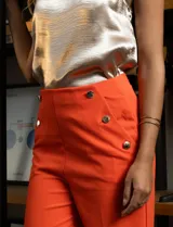 Pantalón naranja de crepe elastizado, corte recto, con bolsillos delanteros y apliques de botones metálicos.