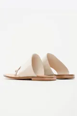 Sandalias chatas de cuero color off-white, con diseño minimalista de tira ancha asimétrica y presilla para el dedo.