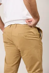 Pantalón chino de gabardina color camel, de corte recto, con bolsillos laterales y traseros, y cierre frontal con botón y cremallera.