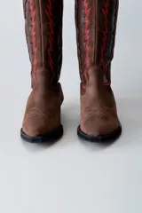 Bota texana de cuero negro con apliques de cuero marrón en los laterales y pespuntes en color crema. De caña media/alta y taco bajo. Diseño calado con motivos geométricos.