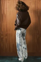 Jeans de tiro medio con corte barrel, confeccionados en algodón con estampado tipo tie-dye en tonos azul y blanco. Presentan diseño de cinco bolsillos, trabillas en la cintura y cierre frontal con cremallera y botón.