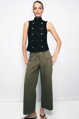 Chaleco negro de cuello subido y manga sisa, con cierre frontal oculto y detalle de botones decorativos metálicos en estilo militar.