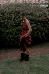 Vestido largo color marrón de crepé plissé, con escote halter adornado con detalles de perlas, silueta fluida y lazo ajustable en la cintura.
