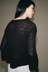 Jersey de punto color negro con cuello redondo y mangas largas terminadas en volantes acampanados.