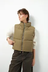 Chaleco puffer color beige, sin mangas, con cuello alto y cierre frontal con cremallera.