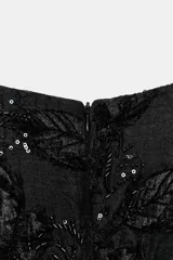 Vestido corto de cuello barco y manga corta abullonada, confeccionado en tejido negro con bordados florales y aplicaciones de abalorios y brillos a tono. Presenta un diseño con volumen en las mangas y cierre de cremallera oculta en la espalda.