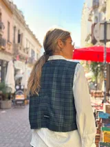 Chaleco de corte clásico con estampado de cuadros en tonos verde oscuro y azul marino. Presenta cierre frontal con botones claros y bolsillos laterales.