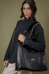 Bolso de hombro confeccionado en cuero vacuno negro, con diseño amplio y minimalista. Cuenta con cierres laterales en los fuelles para ajustar su capacidad y un sobre de cuero desmontable en su interior.