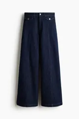 Pantalón de jean de denim azul oscuro, de tiro alto y piernas amplias con corte holgado. Presenta solapas de bolsillo decorativas con botón en el frente y costuras verticales visibles a lo largo de las piernas.