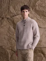 Sweater de punto en color beige, con cuello alto y cierre frontal parcial de botones. Presenta mangas largas con puños acanalados y diseño de corte clásico.