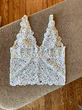 Topcito tipo bralette de encaje blanco con escote en V profundo y tirantes anchos. El encaje es elastizado para un ajuste cómodo.