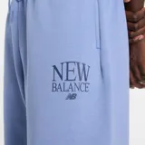 Pantalón de jogging New Balance color azul claro, confeccionado en tejido polar suave. Presenta un corte relajado, cintura elástica con cordón ajustable y puños elásticos en los tobillos. Incluye el logotipo de la marca bordado en la pierna izquierda.