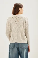 Cardigan de punto color beige con diseño de flores bordadas, escote en V, cierre frontal con botones y mangas largas con puños acanalados.