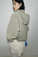 Cazadora de cuello subido con capucha ajustable, manga larga con puños elásticos y bolsillos delanteros con solapa. Presenta bajo elástico y cierre frontal con cremallera oculta y botones a presión.