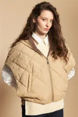 Chaleco de nylon matelaseado color beige, con diseño acolchado de rombos, cierre frontal y corte amplio tipo capa.