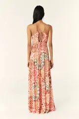 Vestido largo con estampado caleidoscópico en tonos rosa, rojo y verde. Presenta tirantes finos, escote en V, corte imperio y falda con volantes. Incluye detalle de trenzas en el pecho y la cintura que se anudan en la espalda descubierta.