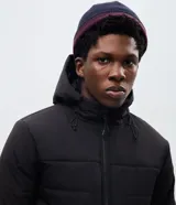 Campera puffer de hombre color verde militar, con capucha integrada, cierre frontal por cremallera y bolsillos cargo frontales. Presenta un diseño acolchado con acabado mate y ajuste en las mangas.