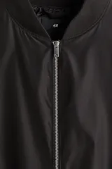 Campera bomber liviana color negro, con cuello, puños y dobladillo acanalados, cierre frontal metálico y bolsillos laterales ribeteados.