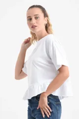 Remera blanca de manga corta y corte holgado, confeccionada en algodón orgánico, con detalle de volado fruncido en el ruedo.