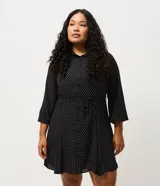 Vestido corto tipo chemise de poliéster con estampado de lunares, cuello camisero con botones frontales, mangas largas con puños elásticos y lazo ajustable en la cintura.
