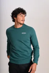 Buzo verde oscuro de cuello redondo, mangas largas con puños elásticos y pequeño estampado ovalado en el pecho.