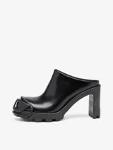 Zuecos negros de cuero con punta redonda y detalle de logo D en la puntera. Taco cuadrado alto y suela track.