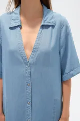 Vestido largo tipo camisero de lyocell, con cuello camisero, cierre frontal de botones, mangas cortas con dobladillo y bolsillos laterales. Presenta un corte holgado y tajos laterales en el ruedo.