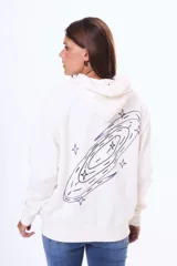 Buzo tipo canguro oversize de color blanco, con capucha y bolsillo frontal. Presenta un estampado artístico de una galaxia con estrellas en tonos violetas en la parte trasera.