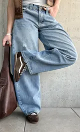 Jean de denim celeste de corte barrel, tiro bajo, con roturas y detalles desgastados en la rodilla.