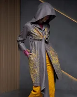 Túnica gris con capucha, confeccionada en gabardina de lana estampada artesanalmente con diseño abstracto en tonos ocre. Presenta dos piezas a modo de bufandas que se anudan en la parte delantera, bolsillos laterales y capucha amplia.