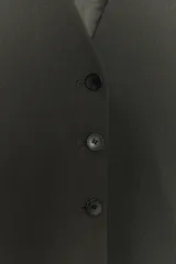 Chaleco de corte sastrero en color gris oscuro, con escote en V, cierre frontal con botones y cintura entallada. Presenta mangas cortas con diseño amplio y forro interior.
