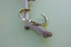 Brazalete rígido abierto de bronce con textura irregular.