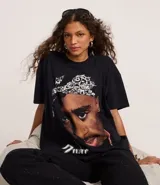 Remera negra de algodón con cuello redondo y manga corta, presentando un estampado grande y detallado del rapero Tupac Shakur con un pañuelo blanco en la cabeza.