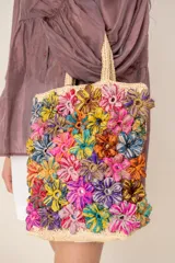 Bolso tipo tote color beige con flores tejidas multicolor en relieve, doble asa corta de mano y diseño rectangular.