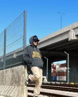 Campera negra con capucha y cierre frontal, con estampado del logo Rona Studio en color naranja en el pecho.