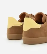 Championes de mujer estilo chuteira, color verde oscuro con detalles en blanco y suela de goma color caramelo. Presentan un diseño de corte bajo con cordones y un logo lateral en forma de arco.