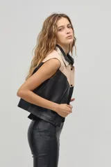 Chaleco de cuero negro y beige con cuello camisero, sin mangas y cierre frontal con botones a presión. Diseño con canesú en contraste y corte recto.