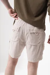 Bermuda color beige de lino tipo cargo, con bolsillos laterales y dos traseros. Cuenta con elástico en la parte de atrás, cierre y botón en el frente.
