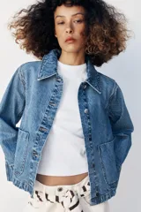 Campera de denim azul con cuello solapa, cierre frontal de botones metálicos, bolsillos delanteros de plastrón y mangas largas acampanadas.