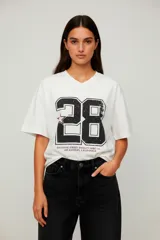 Remera holgada de algodón color blanco, con cuello en V y estampado frontal grande con el número "28" en negro con efecto desgastado y una estrella rosa en el 2. Debajo del número se lee "EXCLUSIVE JERSEY QUALITY RIDE CO. LOS ANGELES, CALIFORNIA".