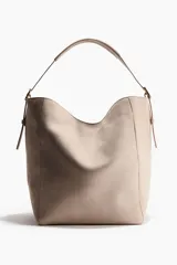 Cartera tipo shopper de gamuza color beige, con diseño estructurado, asa superior ajustable y herrajes metálicos dorados.