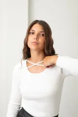 Polera de punto acanalado color blanco, con escote redondo y detalle de tiras cruzadas en el pecho, de manga larga y corte ajustado con ruedo curvo.