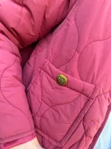 Campera tipo bomber acolchada con diseño de pespuntes ondulados, cierre frontal y bolsillos laterales con botón. Presenta un corte moderno y acabado en color bordo.