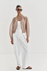 Chaqueta estilo bomber de punto color beige con acabado brillante, cuello redondo, manga larga con puños elásticos y cierre frontal con cremallera.