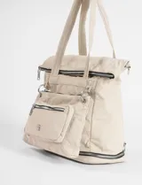 Mochila shopper color beige, confeccionada en poliéster. Presenta un diseño versátil con múltiples cierres, compartimento inferior expandible y un bolsillo frontal removible que funciona como estuche. Incluye correas ajustables y removibles para usar como mochila o bandolera, además de asas fijas para llevar al hombro.