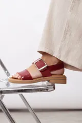 Sandalias de cuero marrón, con diseño de dos fajas amplias, una lisa en la parte delantera y otra superior con hebilla metálica grande y ajustable. Suela plana con plataforma baja y pespunte visible.