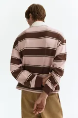 Remera tipo polo de manga larga con diseño a rayas horizontales en tonos rosado y marrón, con cuello blanco de sarga y cierre frontal con botones ocultos.