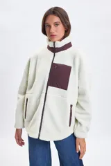 Campera de sherpa color crudo con cuello alto, cierre frontal completo y detalles en color bordó. Presenta un bolsillo frontal con cierre y dos bolsillos laterales, todos con terminaciones en contraste.