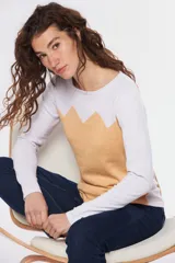 Buzo de tejido de punto con diseño combinado en bloques de color, presentando un panel frontal en tono beige con terminación en zigzag y mangas y parte superior en color blanco con efecto jaspeado.